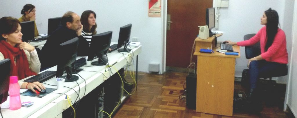 Participantes del taller Guaraní 3 de 2017 en el aula de la academia del CeSPI sentados en escritorios contiguos, consultando las computadoras. Al frente una mujer integrante del área de Sistemas Académicos coordinando el taller.